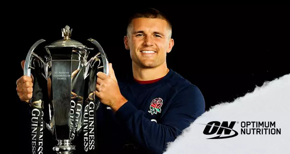 Henry Slade holding the Guinness Six Nations trophy, wearing an England rugby top next to the Optimum Nutrition logo.