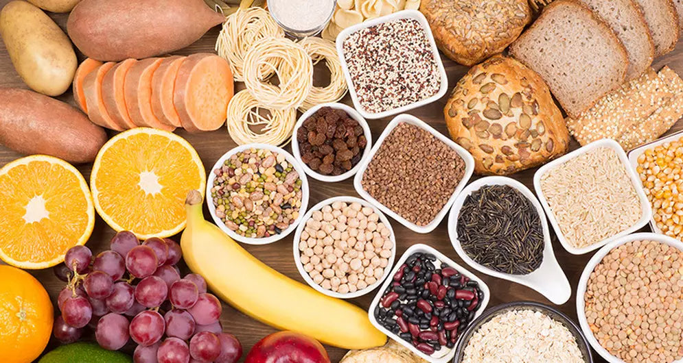 Assorted high-fibre foods including fruits, legumes, grains, and wholemeal bread displayed on a wooden surface.