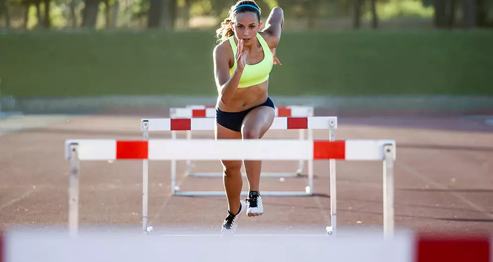 Female athlete sprinting and jumping over hurdles on a track, showcasing speed, power, and explosive performance.
