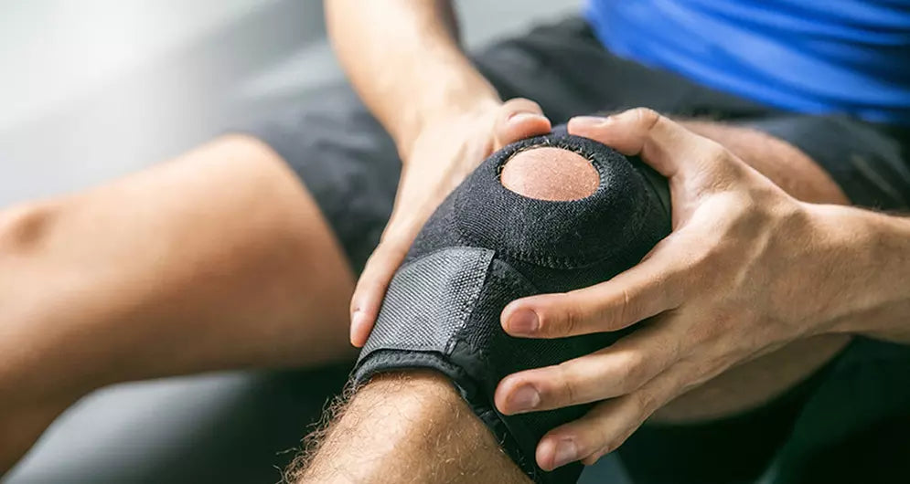 Man wearing a knee brace and holding his injured leg during recovery or post-injury rehabilitation.