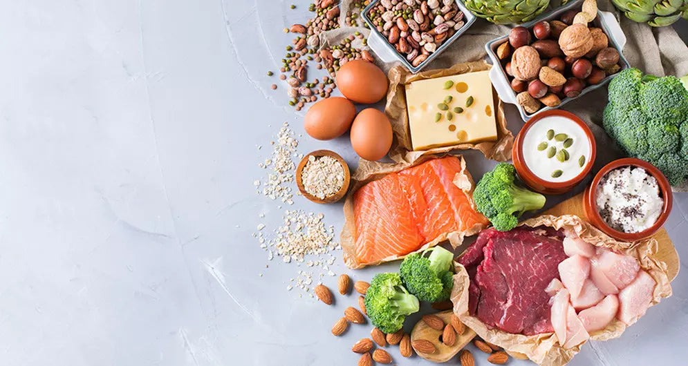 High-protein foods including salmon, beef, chicken, eggs, nuts, cheese, yogurt, legumes, oats, and broccoli.