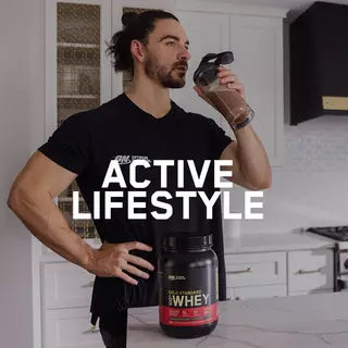 Man drinking a protein shake next to a container of Gold Standard Whey protein powder on a kitchen counter