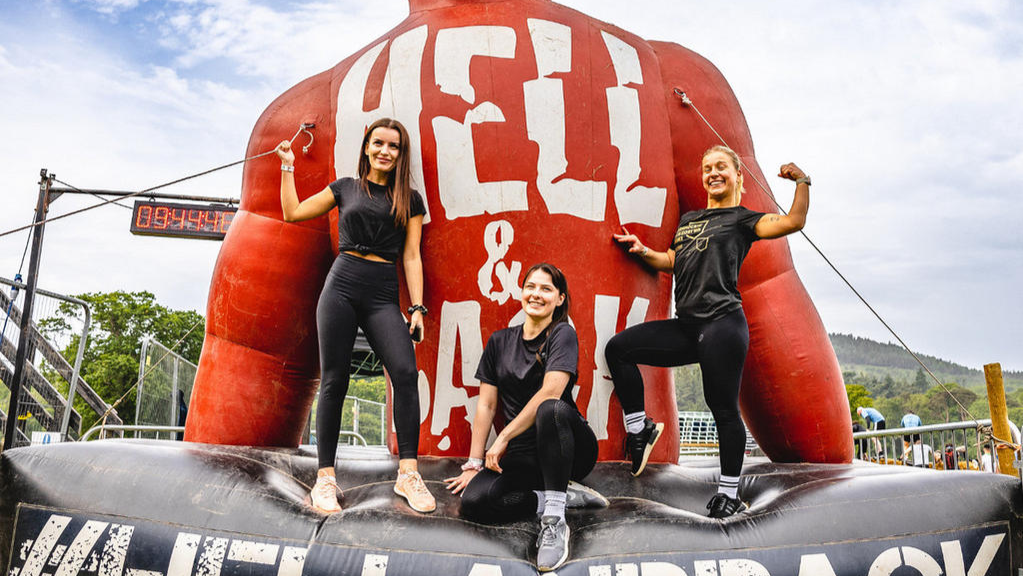 Three people posing in front of a large inflatable obstacle at an outdoor event