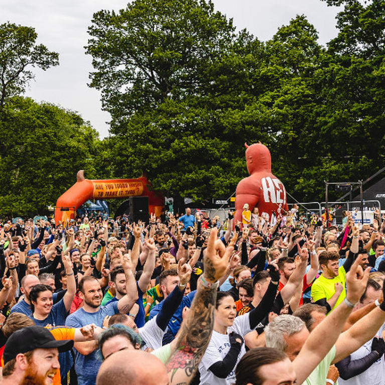 A large group of people gathered outdoors, some with raised hands, possibly participating in a fitness or sports event