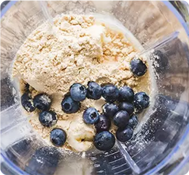 Blender with protein powder, blueberries, and banana slices for a protein shake preparation