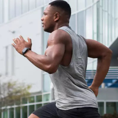 A man running outdoors, wearing a sleeveless athletic top and shorts, demonstrating fitness and high-intensity workout