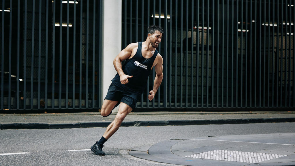 Man running on a street corner wearing athletic gear, possibly after consuming a pre-workout supplement
