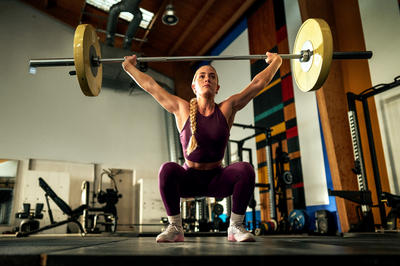 A person performing an overhead squat with a barbell in a gym setting