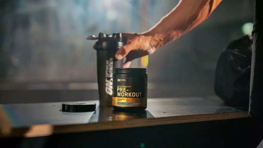 Optimum Nutrition Gold Standard Pre-Workout supplement container next to a shaker bottle on a table