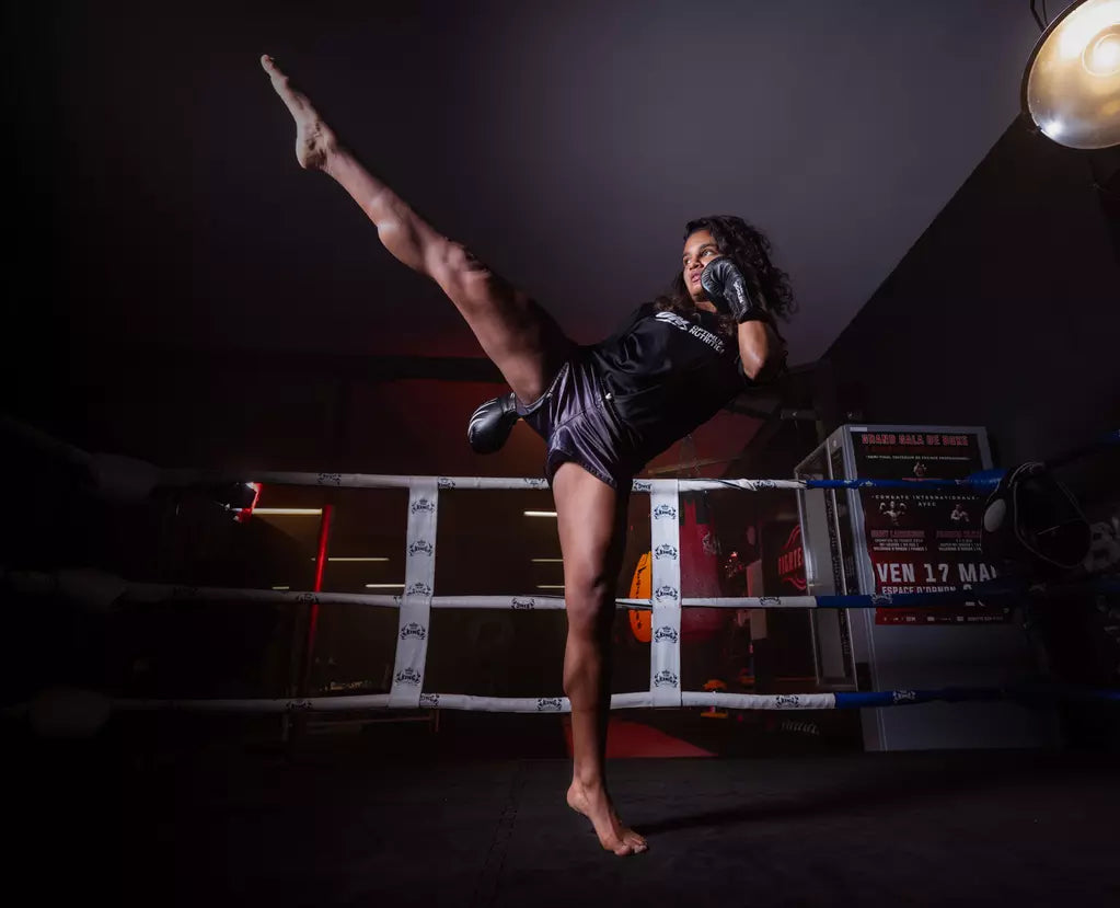 A person practicing a high kick in a boxing ring, wearing boxing gloves and athletic gear