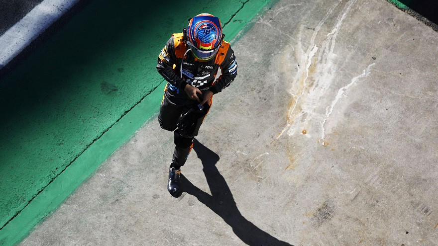 A person in racing gear and helmet walking on a concrete surface