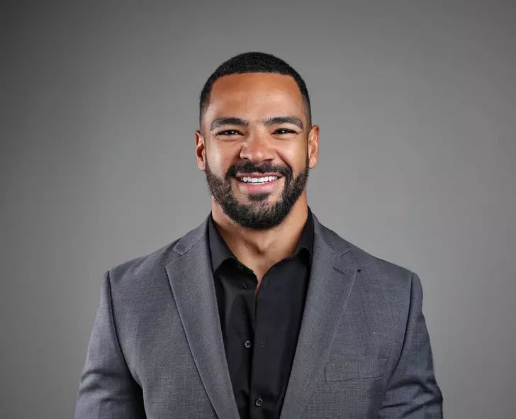 A person smiling, wearing a suit and shirt, against a plain background
