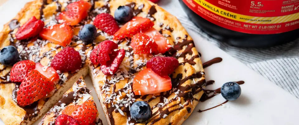 Waffle topped with strawberries, raspberries, blueberries, and chocolate drizzle next to a container of protein powder