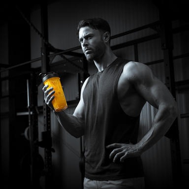 Man holding a shaker bottle in a gym setting, likely containing a protein or amino energy drink