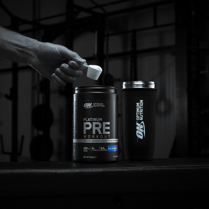 Optimum Nutrition Platinum Pre-Workout supplement container with a scoop, next to an Optimum Nutrition shaker bottle