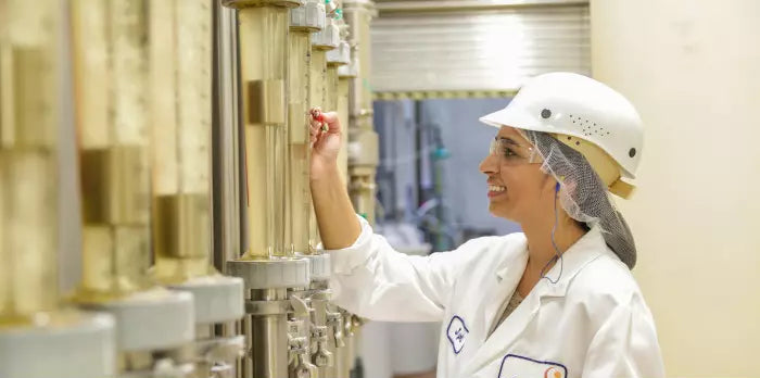 A person in a lab coat and helmet working with industrial equipment, possibly involved in supplement or protein powder production