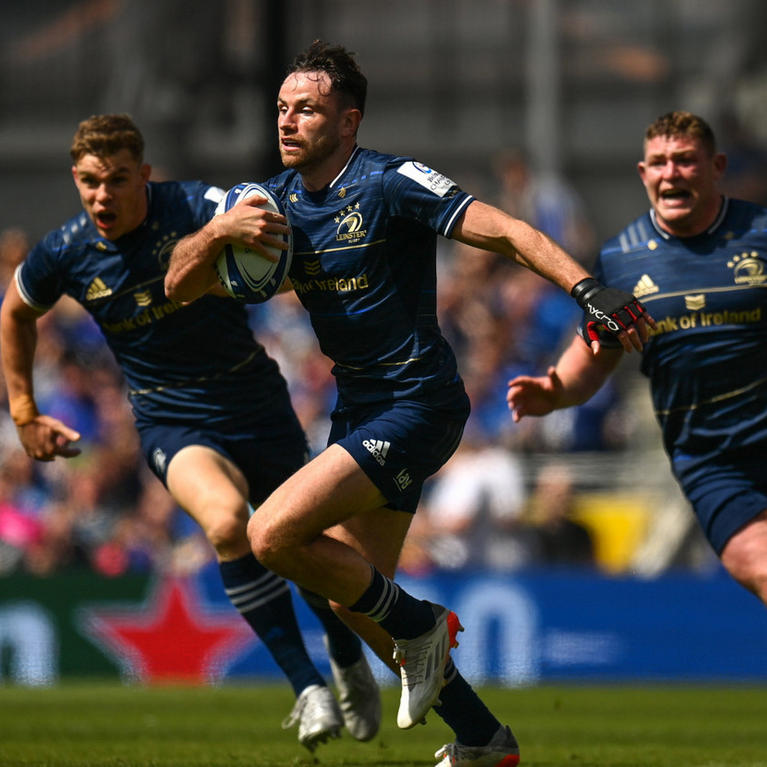 Rugby player in action, holding a ball, with teammates running alongside on a field