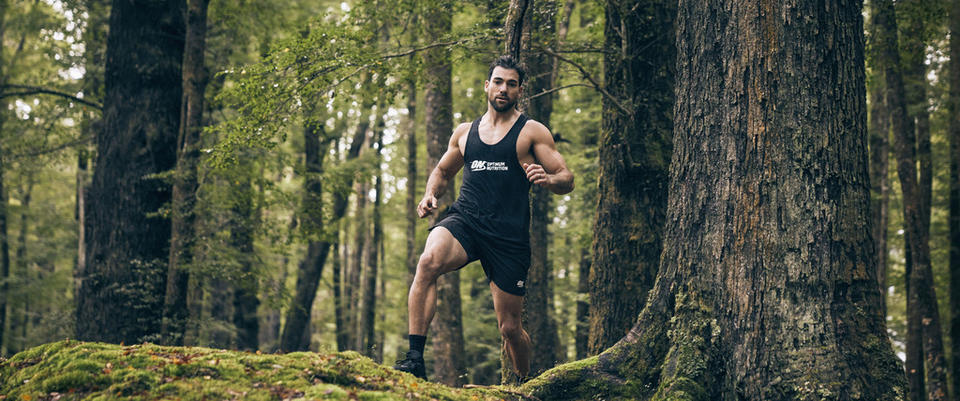 Man exercising in a forest, wearing a tank top with a fitness logo