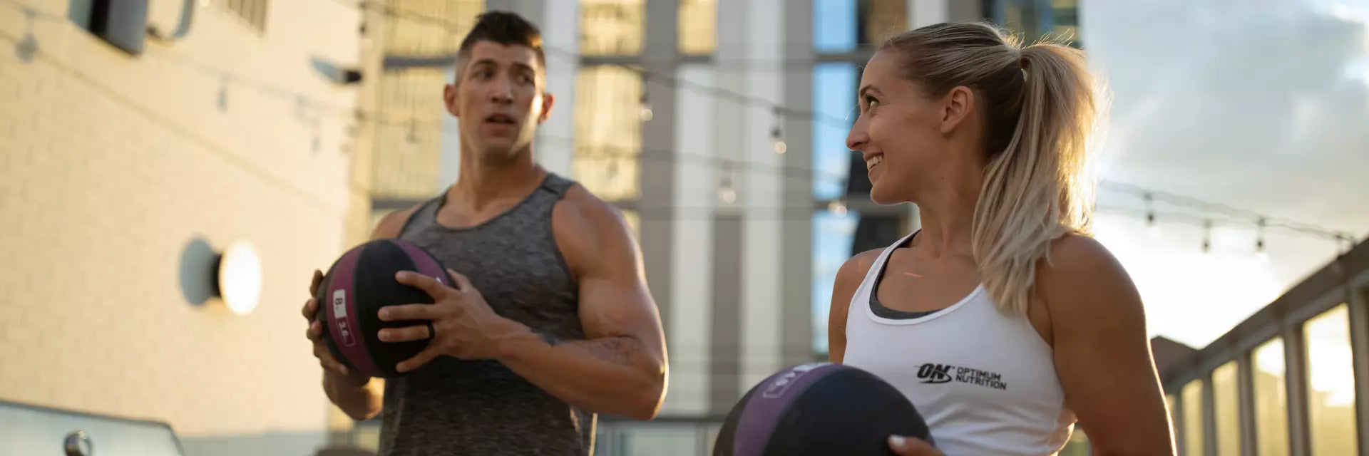 Two people holding medicine balls, wearing athletic clothing with "ON" branding, likely engaging in a workout