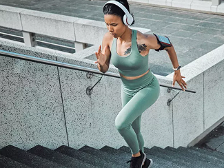 A person running up outdoor stairs wearing athletic clothing and headphones, possibly engaging in a workout or fitness activity