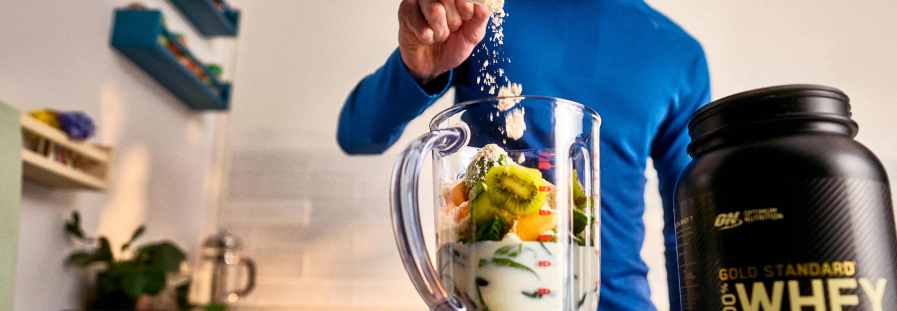 Person preparing a protein shake with Optimum Nutrition whey protein in a kitchen.