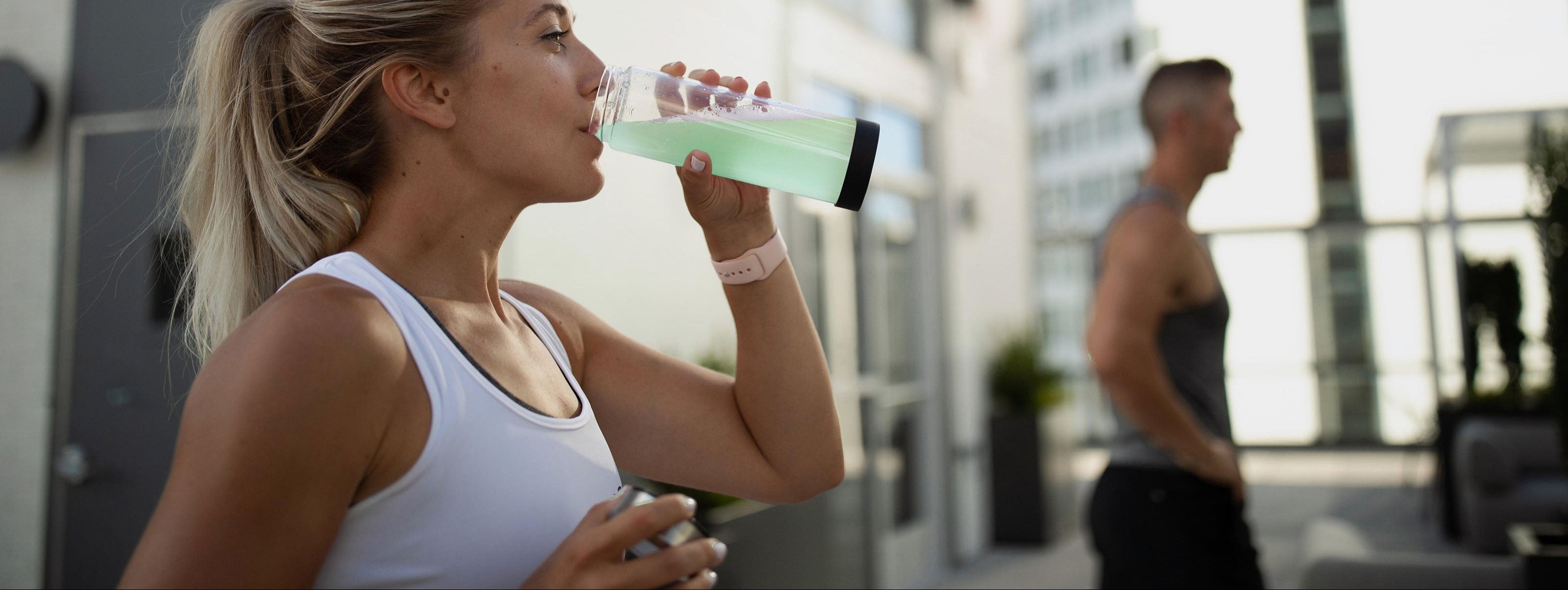 Woman drinking from a shaker bottle, possibly containing an amino energy drink, during a workout session