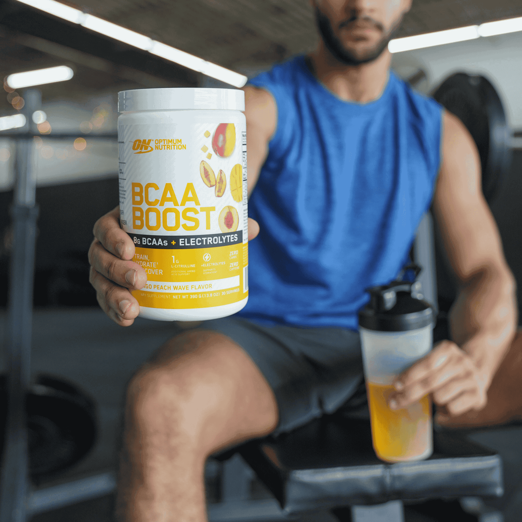 Optimum Nutrition BCAA Boost, Peach Wave flavor, with electrolytes, held by a person in a gym setting
