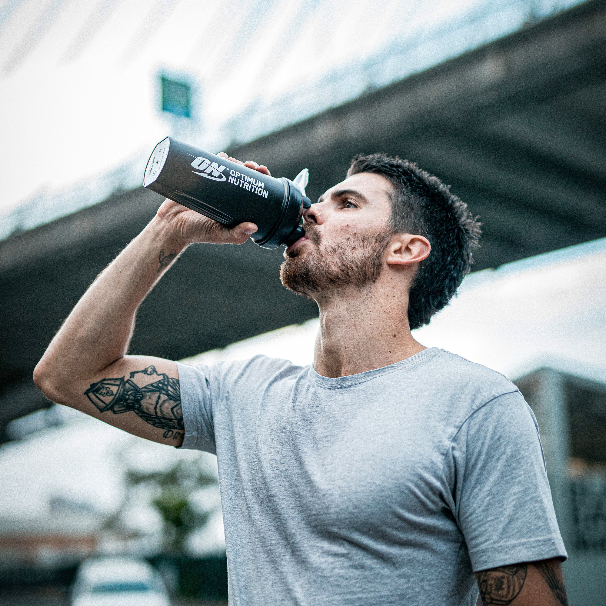 Man drinking from an Optimum Nutrition shaker bottle, likely containing a supplement such as amino energy or protein powder
