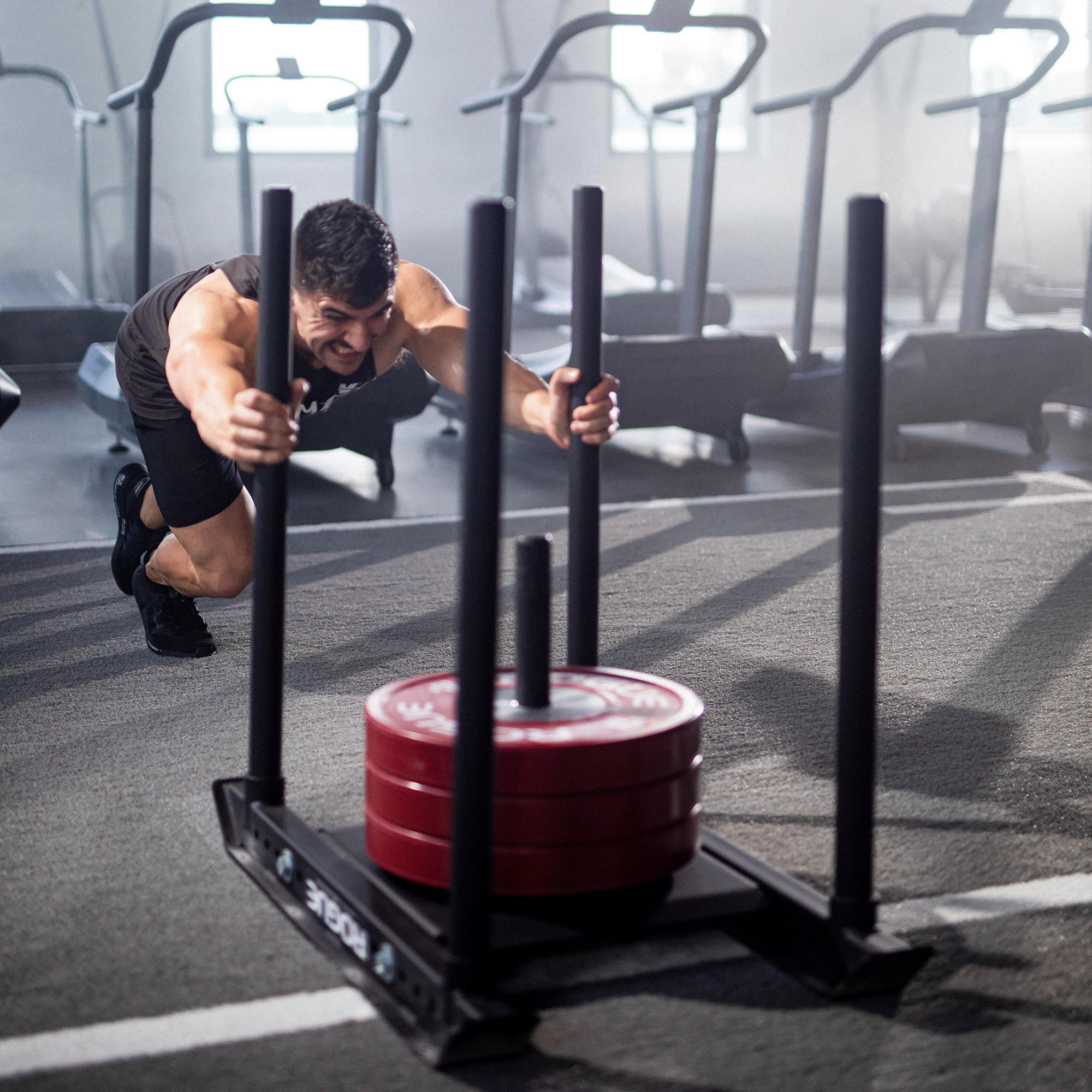 Man pushing a weighted sled in a gym, engaging in high-intensity workout for muscle building