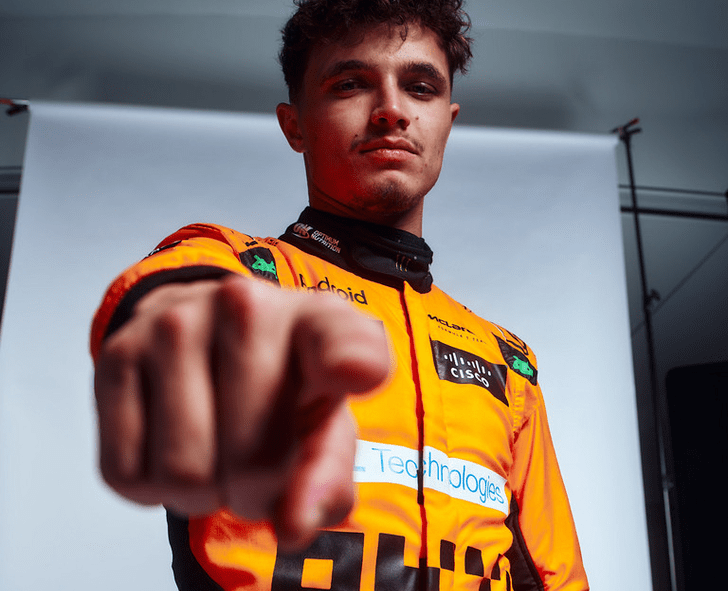 Lando norris wearing an orange racing suit with visible branding, pointing forward