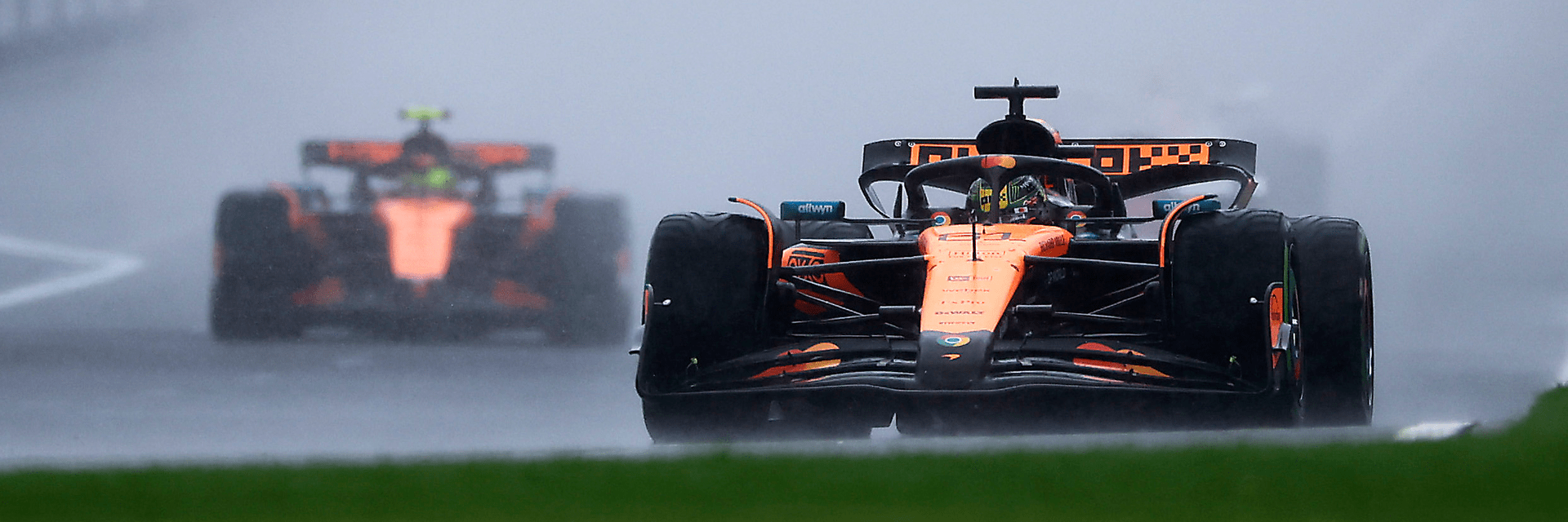Two Formula 1 cars racing on a wet track, with one car leading closely followed by another