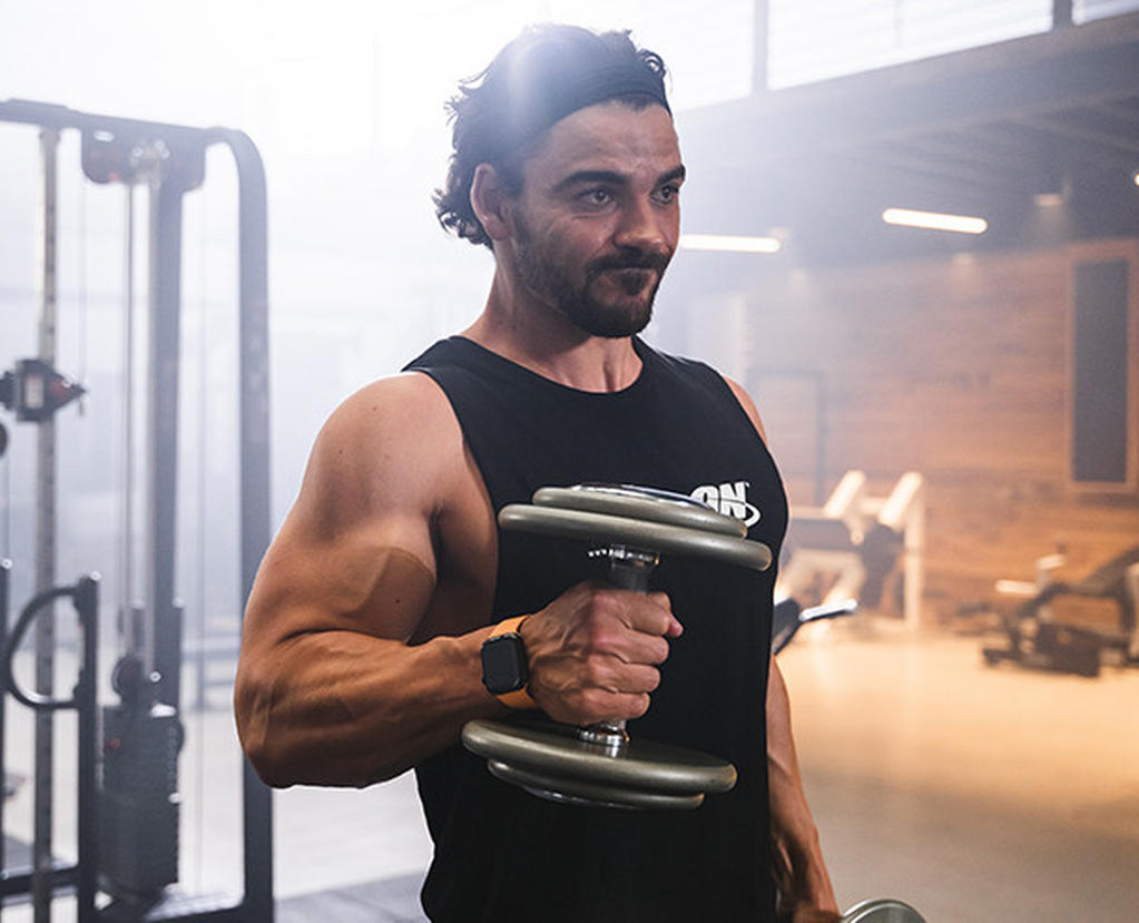Man lifting a dumbbell in a gym setting, wearing an ON-branded tank top