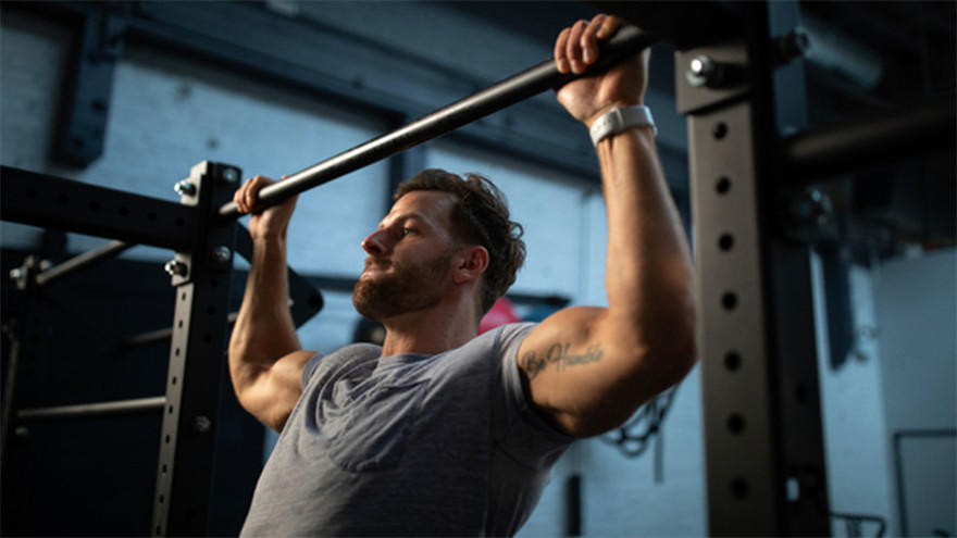 A person performing a pull-up on a gym bar, focusing on strength training and muscle building
