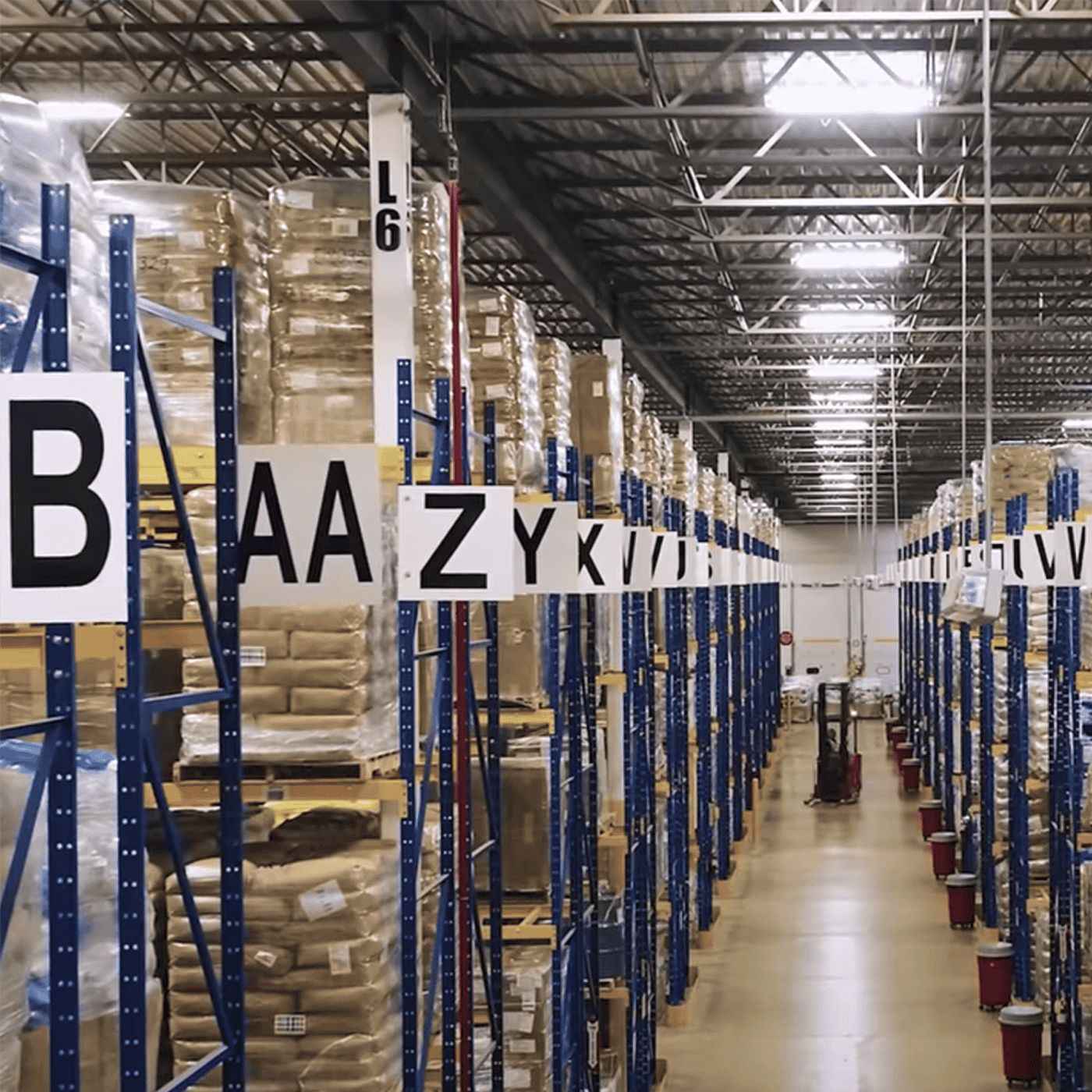 Warehouse interior with tall shelving units filled with stacked boxes, labeled with large letters for organization