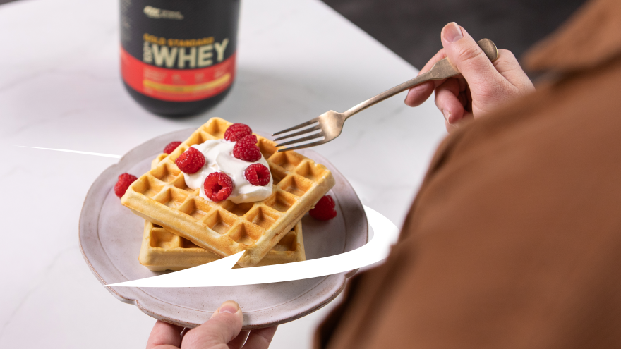 Gold Standard Whey protein powder container next to a plate of waffles topped with whipped cream and raspberries