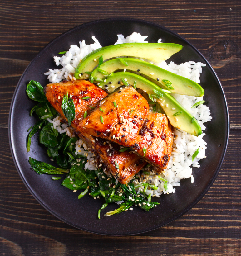 Grilled salmon with avocado slices, served on a bed of rice and spinach, garnished with sesame seeds