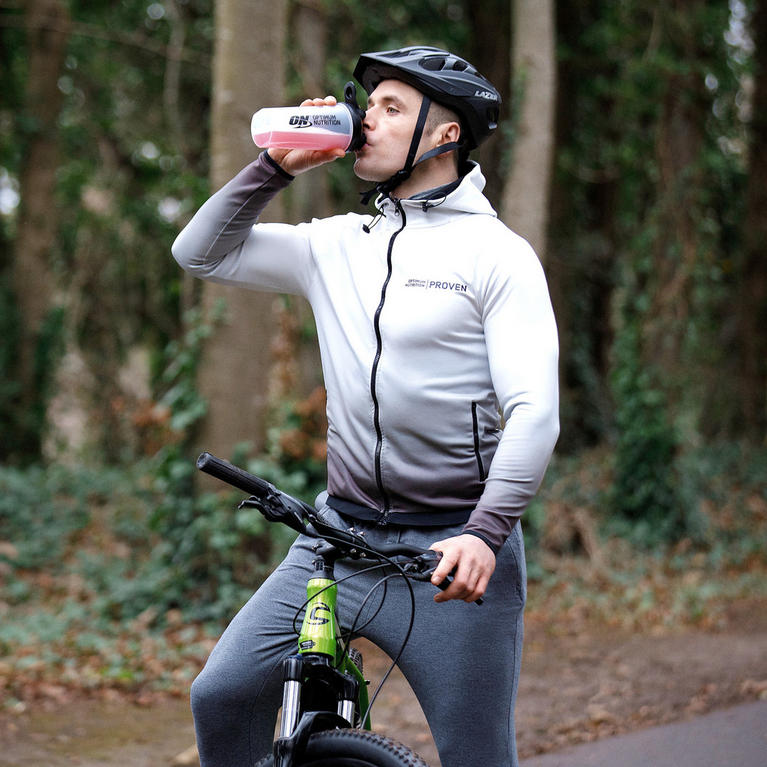 Cyclist drinking from a USN-branded bottle while resting on a mountain bike in a forest setting