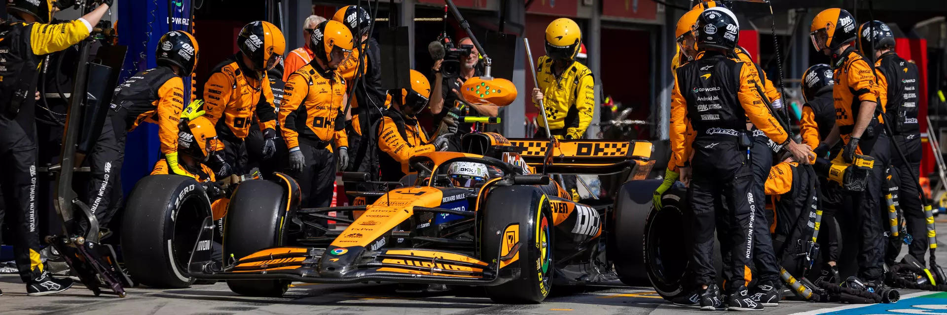 A Formula 1 race car in the pit stop surrounded by a team of mechanics performing maintenance and refueling tasks