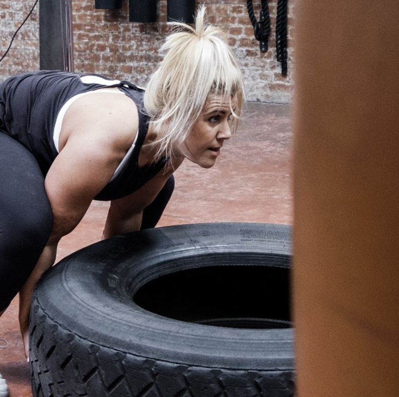 A person engaging in a high-intensity workout, lifting a large tire in a gym setting