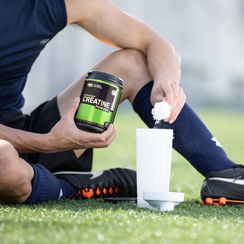 man putting a scoop of creatine in a shaker while on pitch