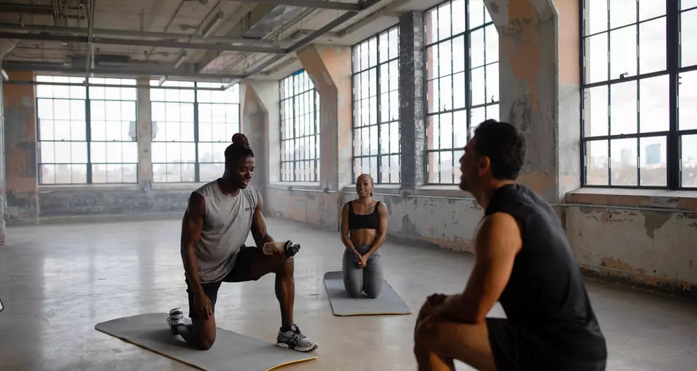 Groupe de sportifs faisant des exercices au sol dans une salle lumineuse pour améliorer la mobilité et la récupération.