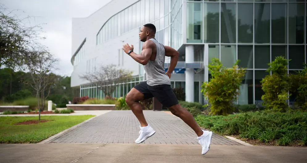 Athletic man sprinting outdoors in front of a modern glass building, showcasing speed, power, and performance training.