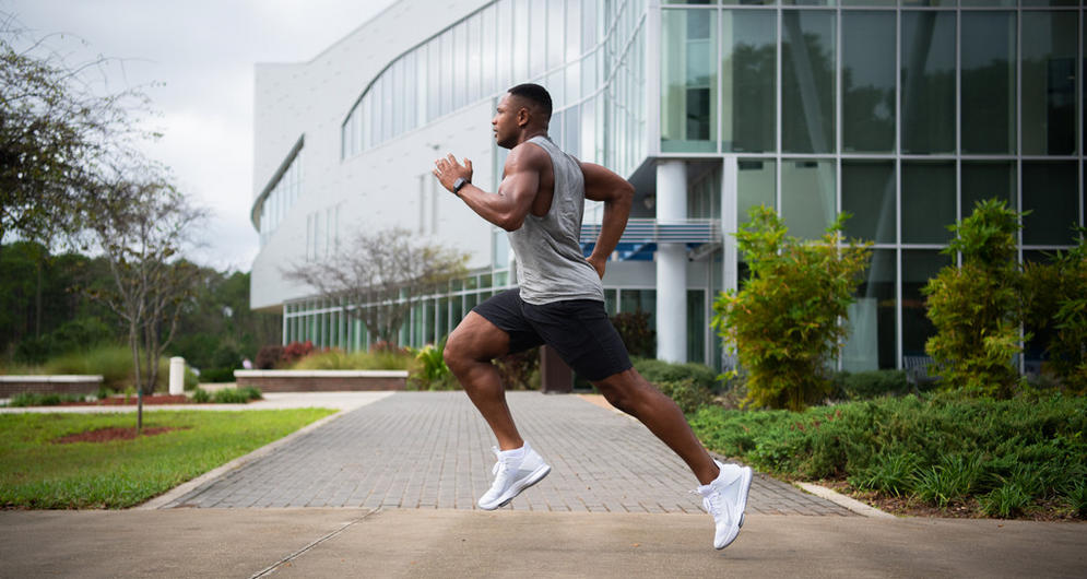 Man running in tank top and shorts in front of glass building
