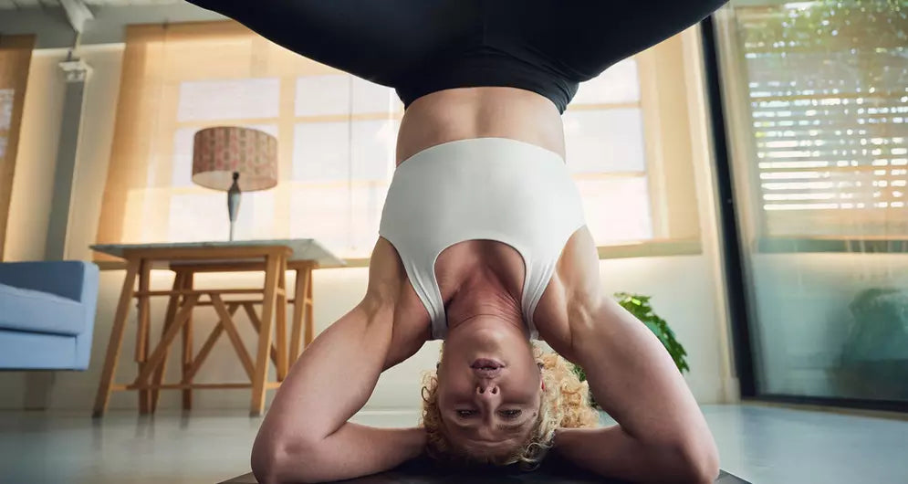 Woman in a white sports bra holding a headstand indoors, demonstrating strength, balance, and core control.