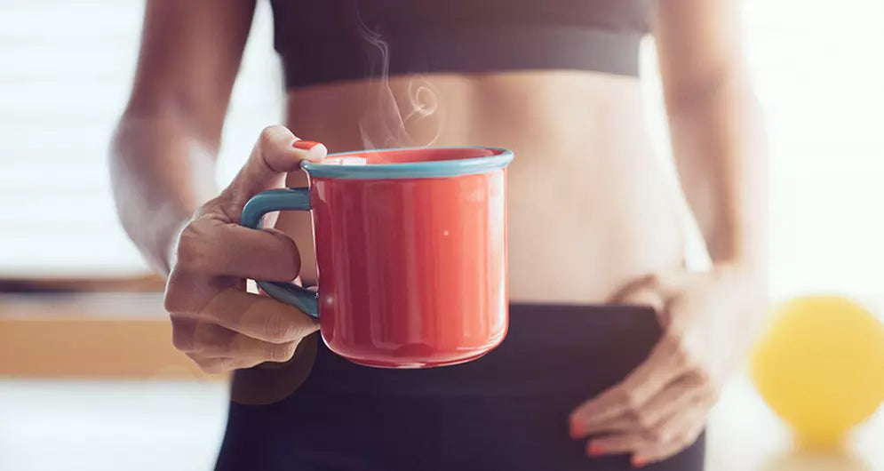 Woman in workout clothes holding a steaming mug, visually linking caffeine and fitness in a morning setting.