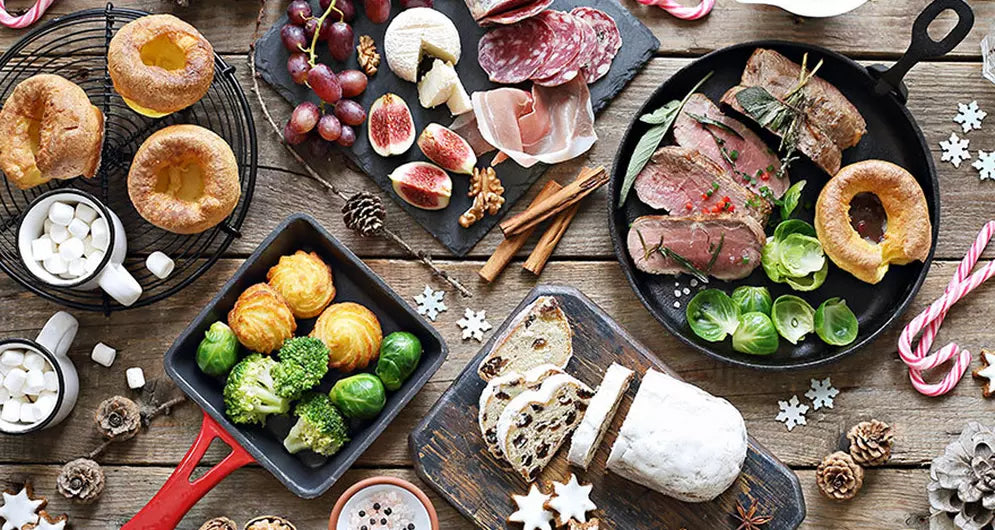 Festive holiday meal with roasted meat, cheese, figs, vegetables, Yorkshire puddings, and Christmas decorations.
