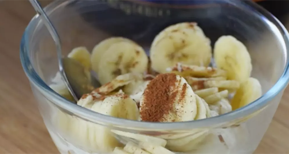 Gold Standard 100% Casein banana yogurt in a glass bowl, topped with banana slices and cinnamon, with a spoon inside.