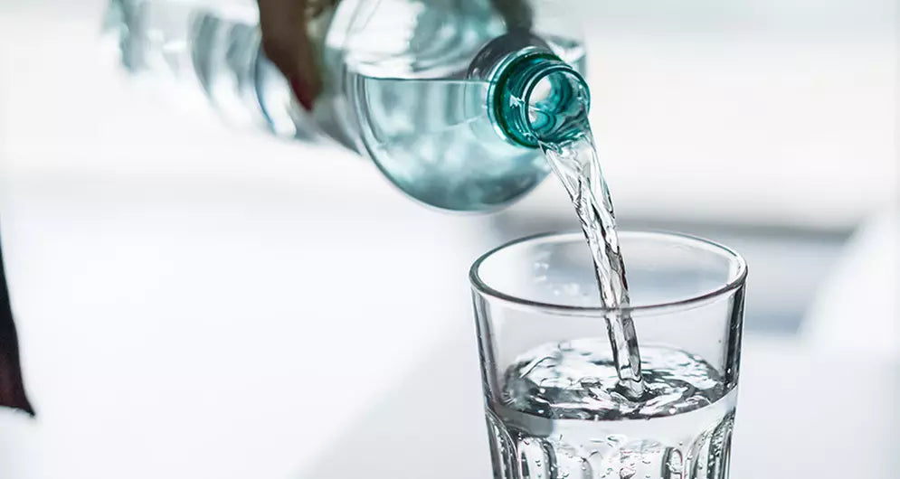 Close-up of water being poured from a plastic bottle into a clear glass, highlighting hydration and fluid intake.