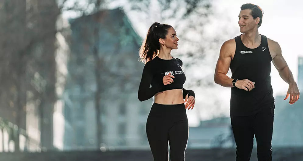 Fit man and woman jogging outdoors in athletic wear, smiling at each other during a morning run.