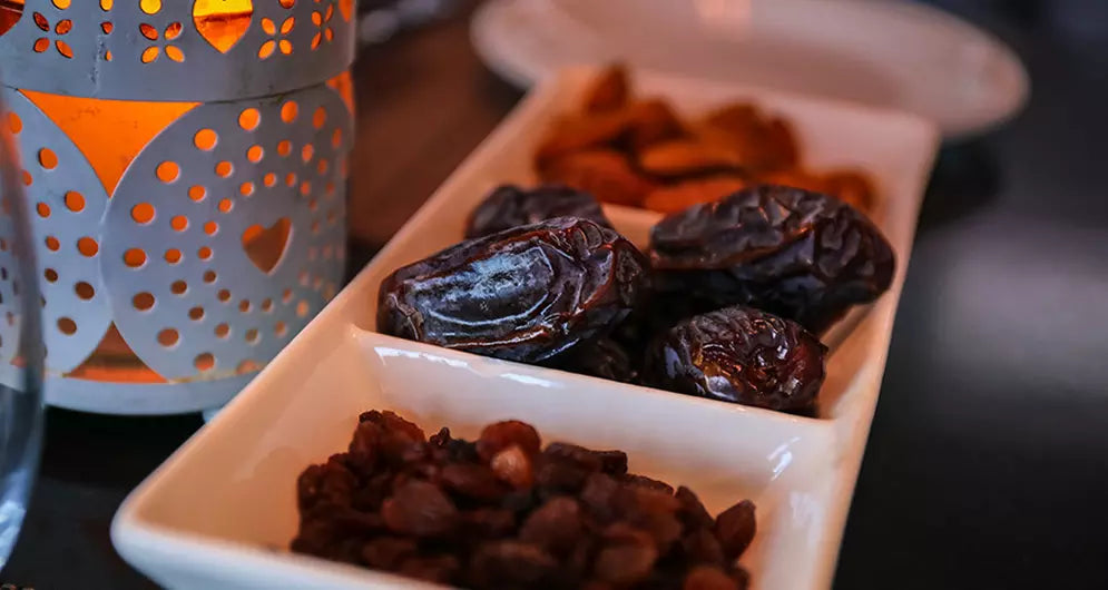 Close-up of dates, raisins, and dried apricots in a white dish beside a decorative lantern.